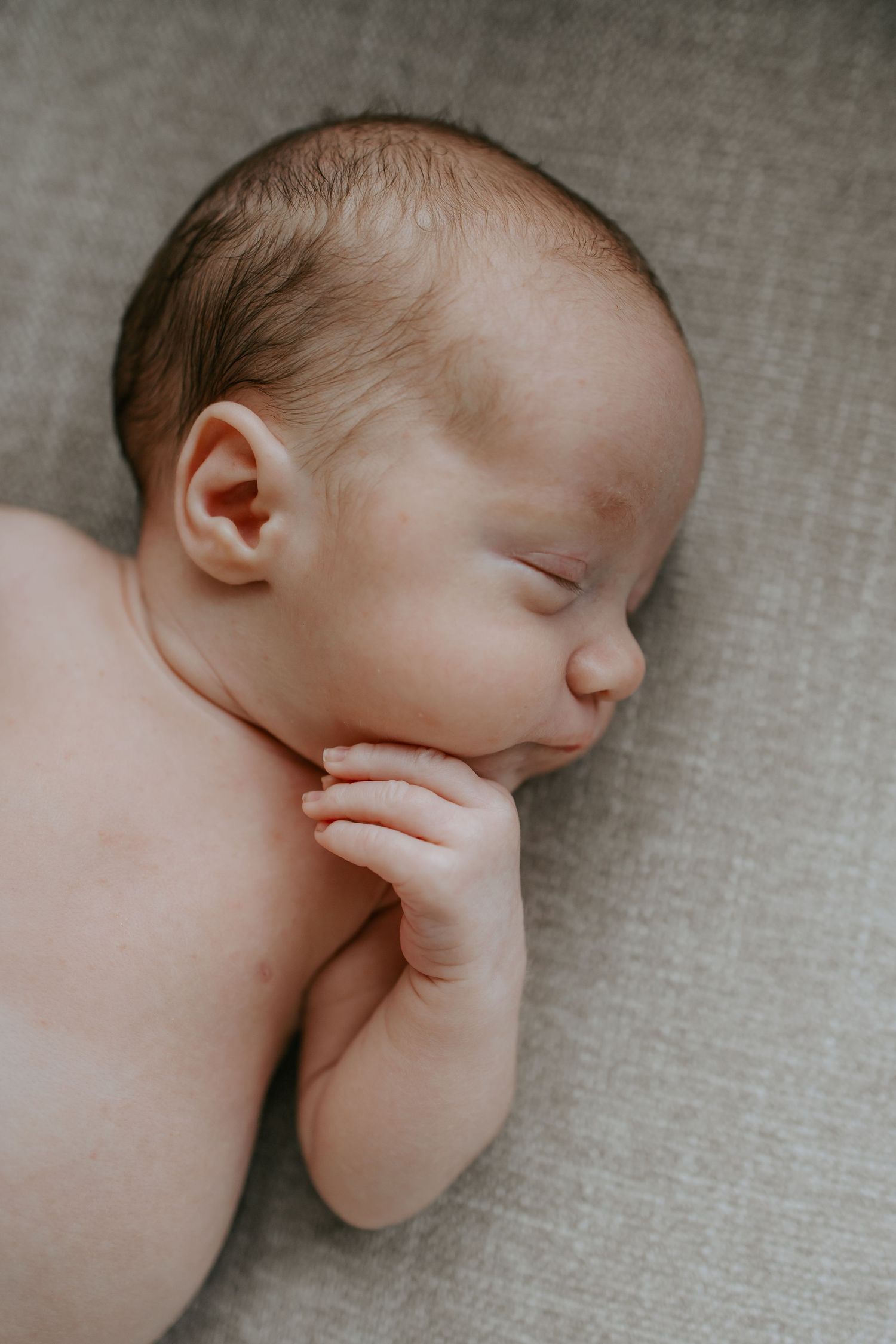 Peaceful sleeping newborn baby lying on grey textured surface, side profile view.