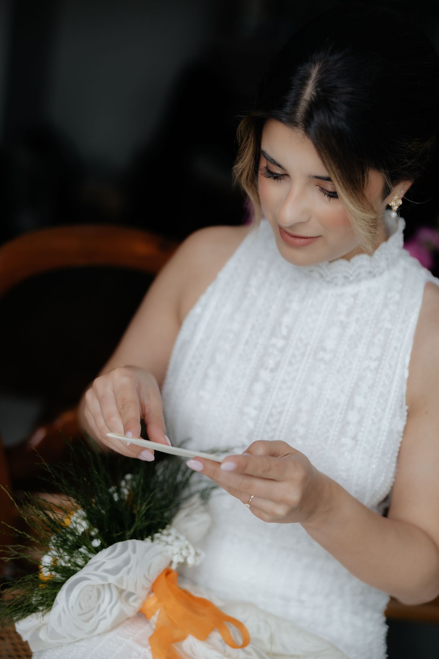 Bride in a white knit wedding dress reading a small card next to a floral bouquet.