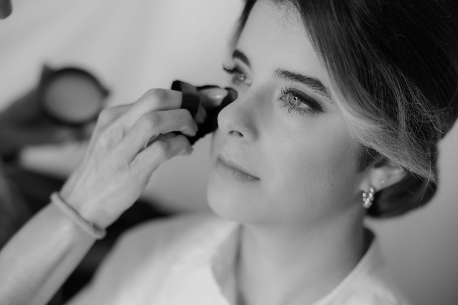 Black and white close-up of a bride having eye makeup applied by a professional makeup artist.