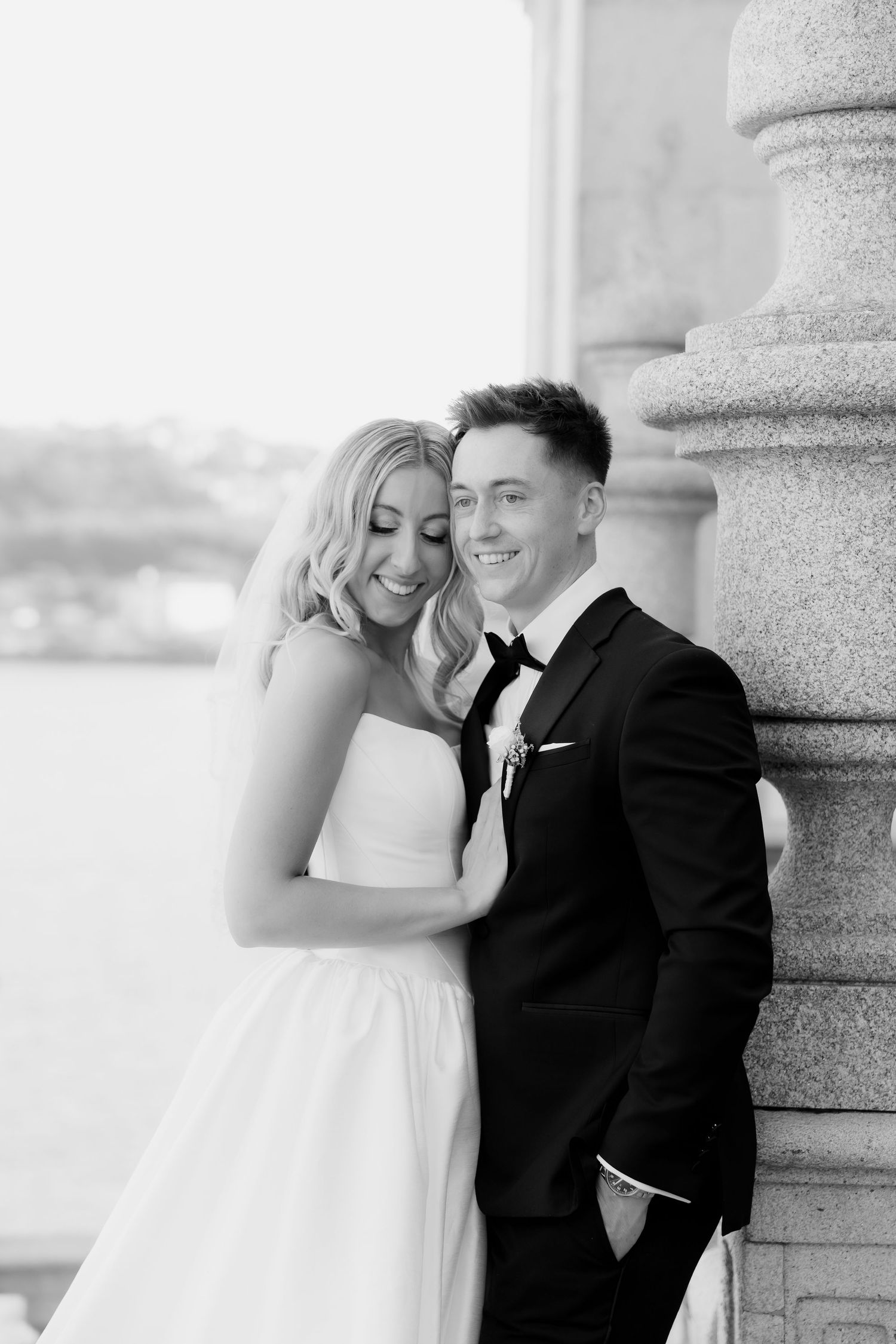 A romantic black and white wedding photo series showing a couple embracing against stone pillars.