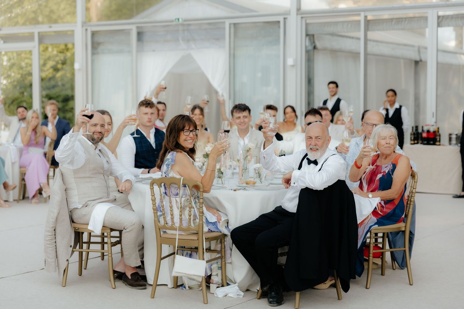 Wedding reception guests seated at elegant white tables in a bright, airy venue with natural lighting and rustic decor.