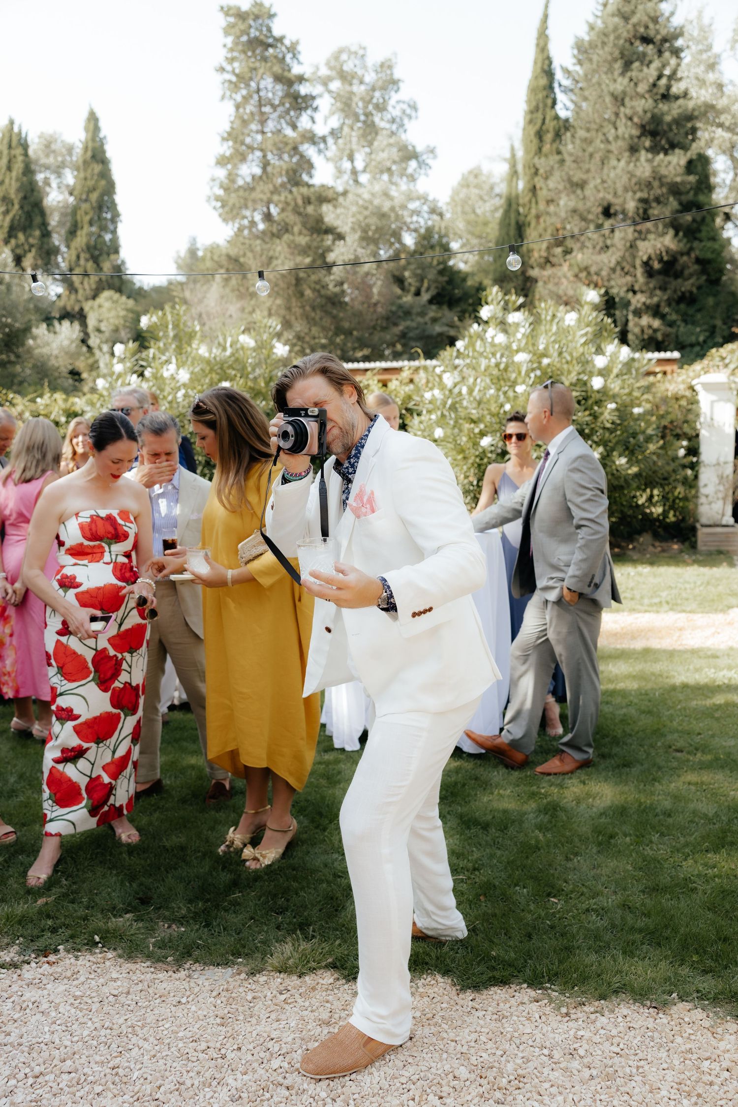 Wedding guests in colorful attire enjoying outdoor celebration on grassy lawn.
