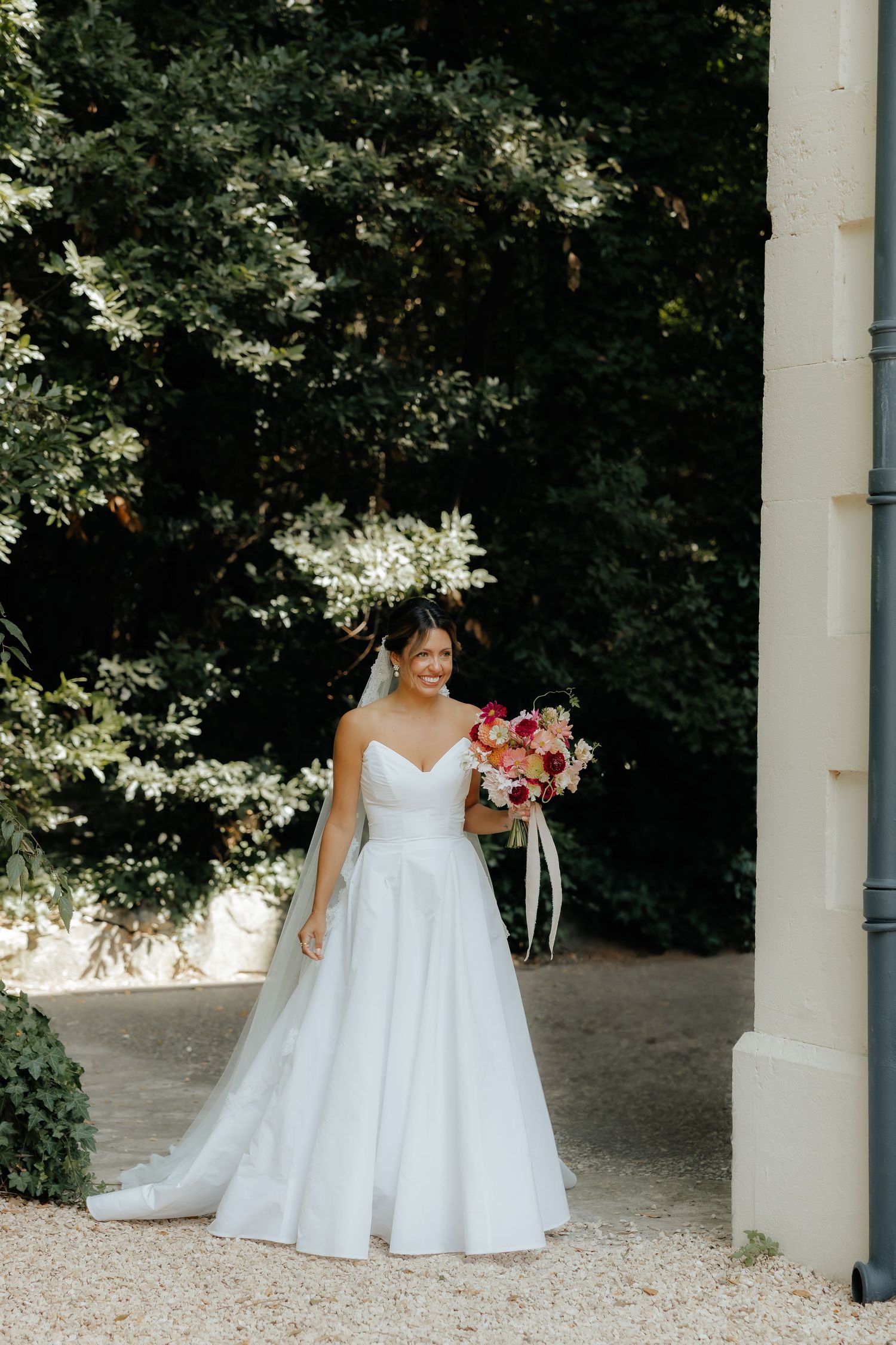Bride in flowing white gown walking through an elegant outdoor colonnade.