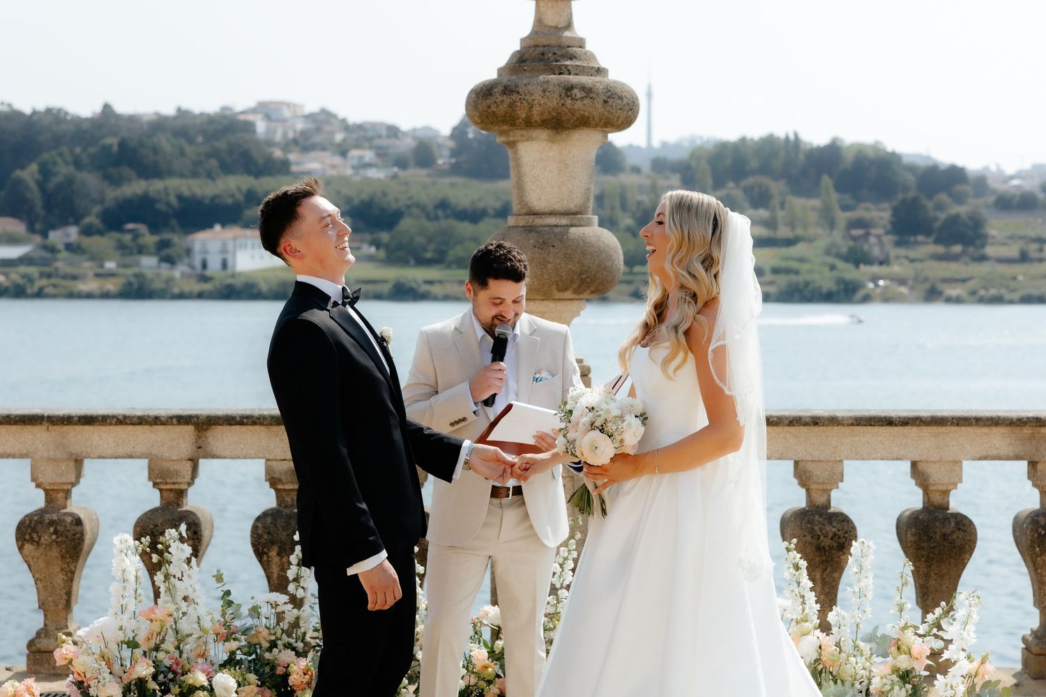 Bride and groom exchange vows at outdoor waterfront wedding ceremony with floral arrangements.