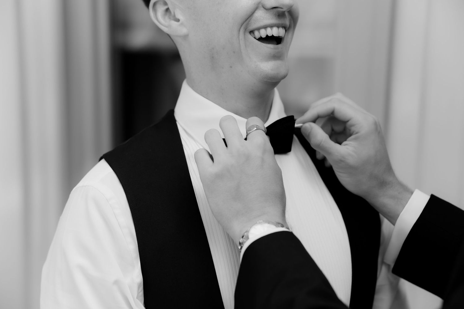 A group of men in tuxedos and bow ties share a candid laughing moment together at a formal event.