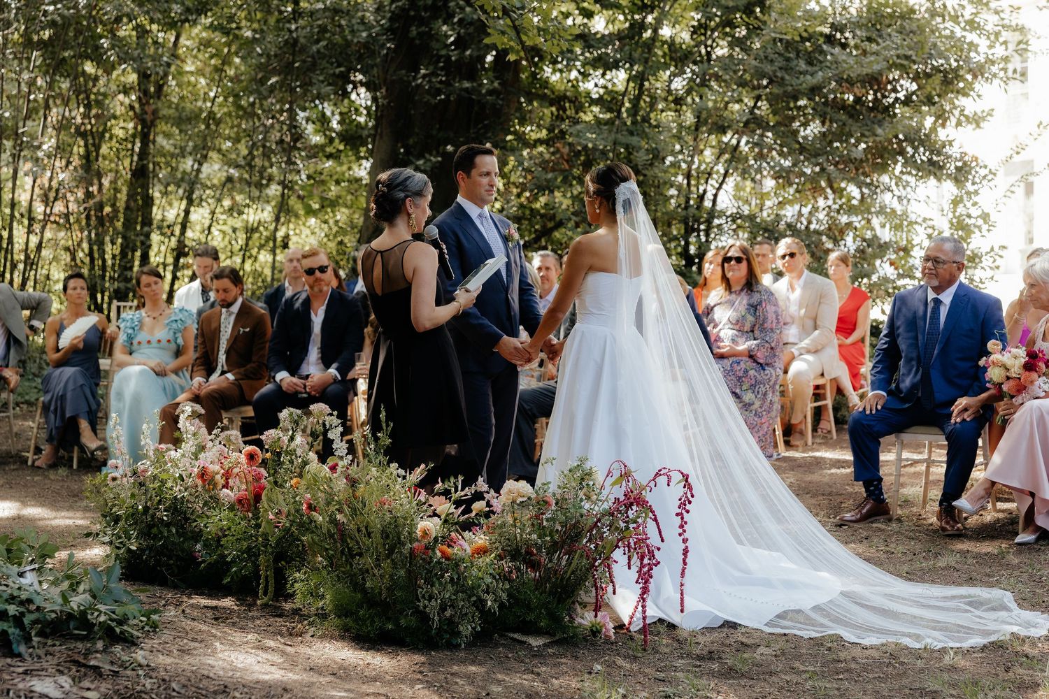 An outdoor wedding ceremony setup with white chairs and floral arrangements under trees.