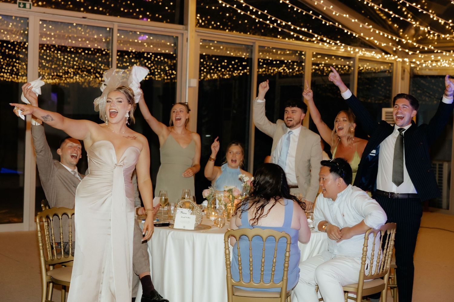 Wedding guests dance and celebrate under twinkling string lights at an evening reception.