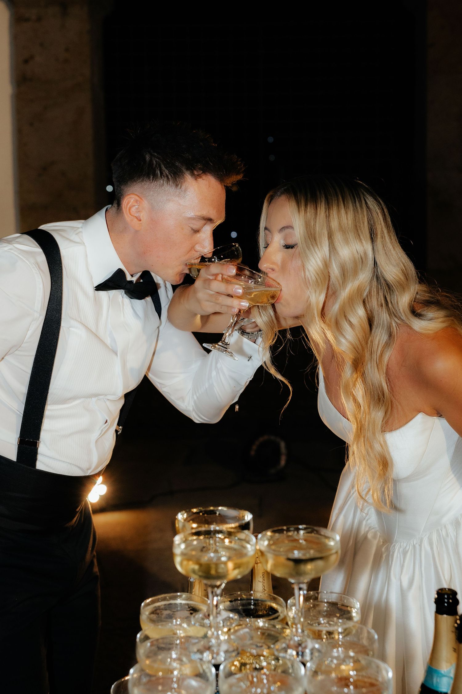 Bride and groom sharing a champagne coupe glass together at their wedding reception celebration.