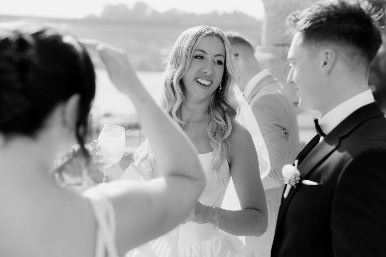 Black and white photo of joyful bride laughing with groom in tuxedo during outdoor wedding celebration.