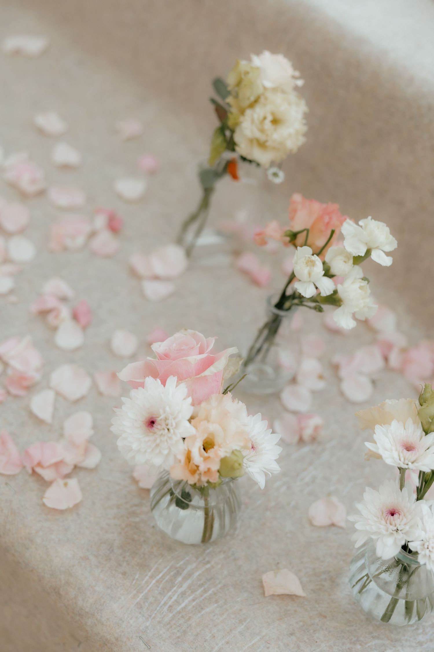 Delicate wedding ceremony decor with small glass bud vases of pink roses and white flowers on linen.