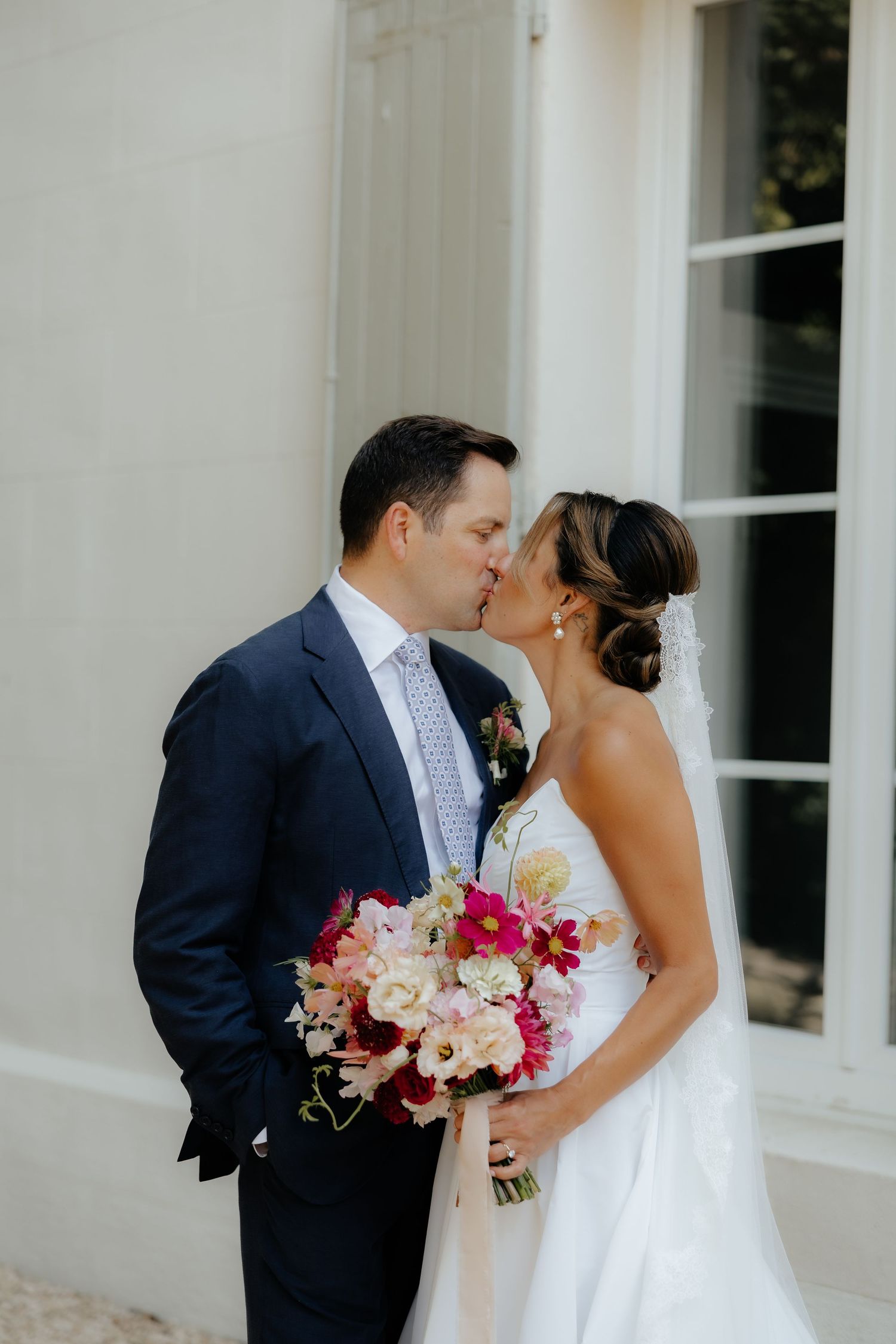 Tender wedding day kiss captured in front of classic white architecture.