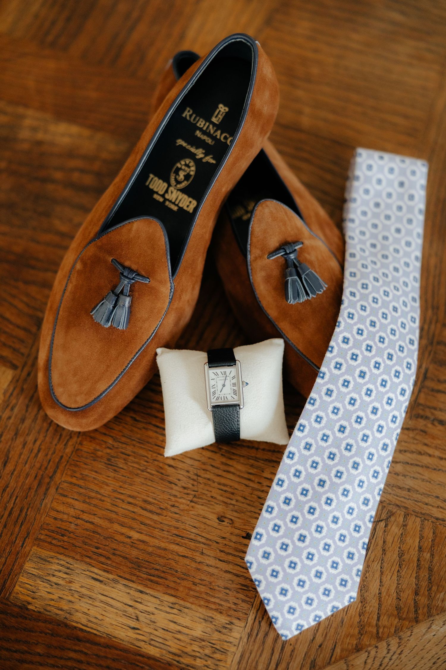 Brown leather loafers and a light blue patterned tie arranged on a wooden surface.