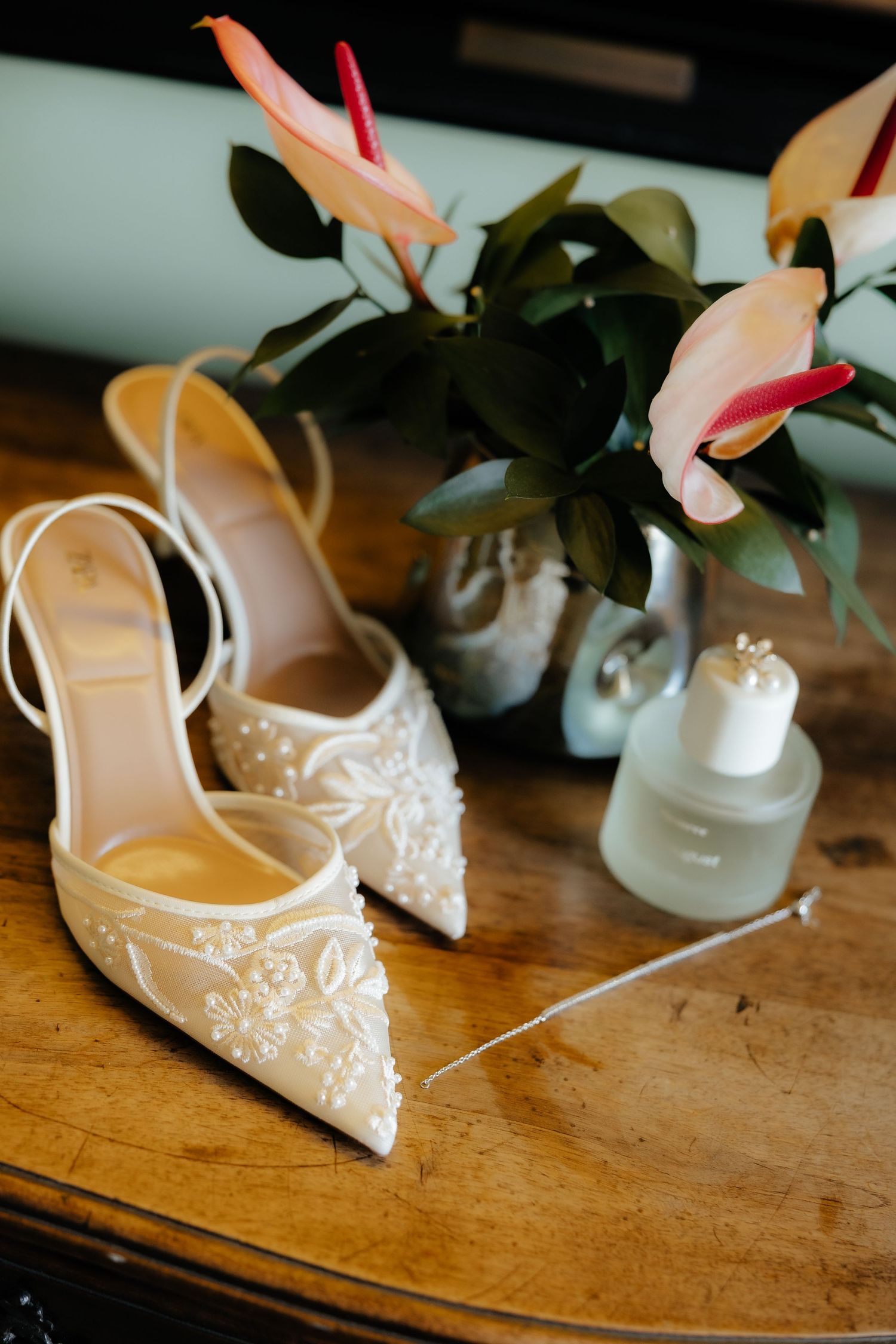 Elegant white lace bridal shoes with delicate embellishments displayed on a rustic wooden surface.