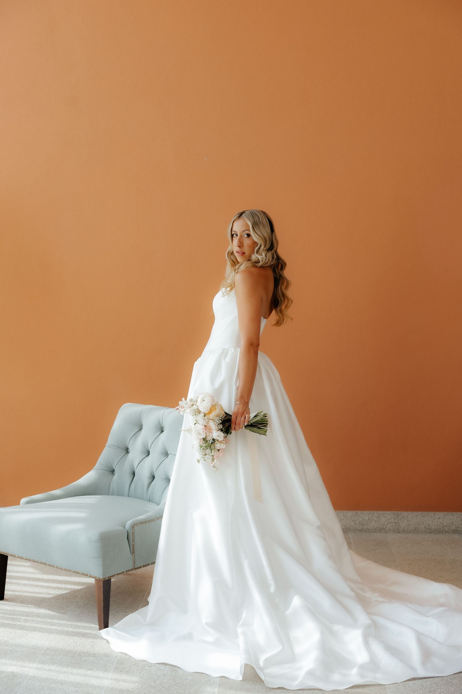 A series of wedding dress photos showing a flowing white gown with train against a peach wall and blue accent chair.