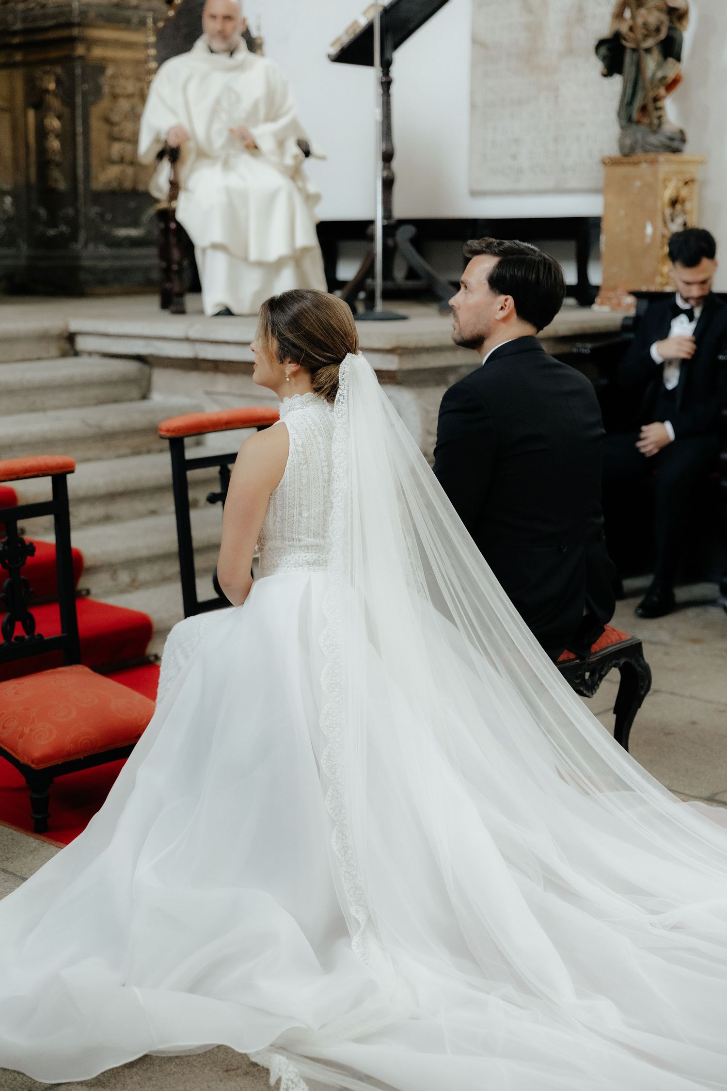 Bride and groom kneel before priest during Catholic wedding ceremony at altar.