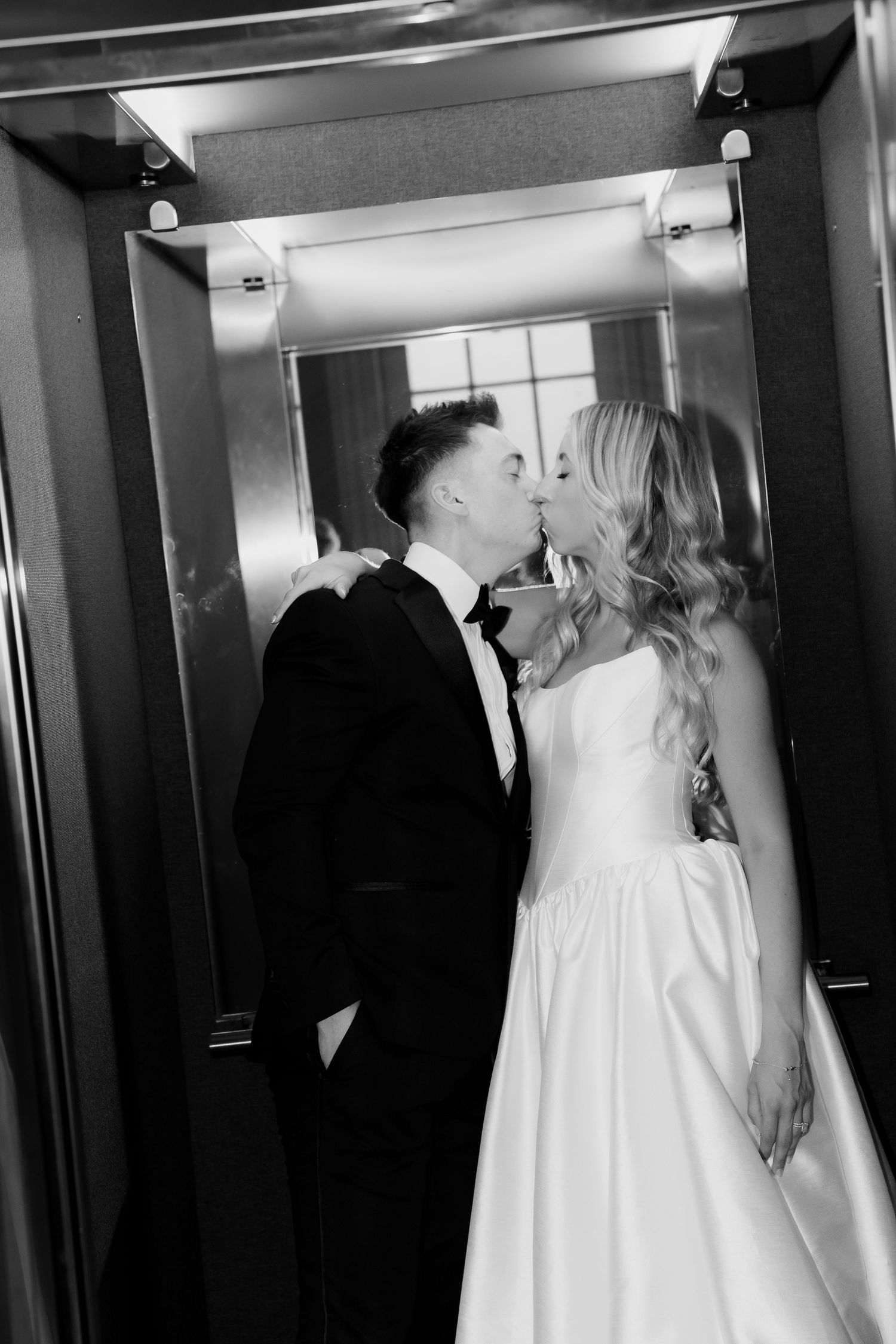 Black and white photo of bride and groom sharing a kiss in an elevator on their wedding day.