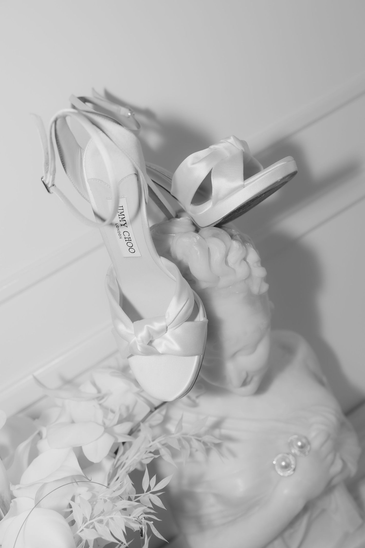 Black and white photo of Jimmy Choo bridal heels resting on a wedding dress with floral details.