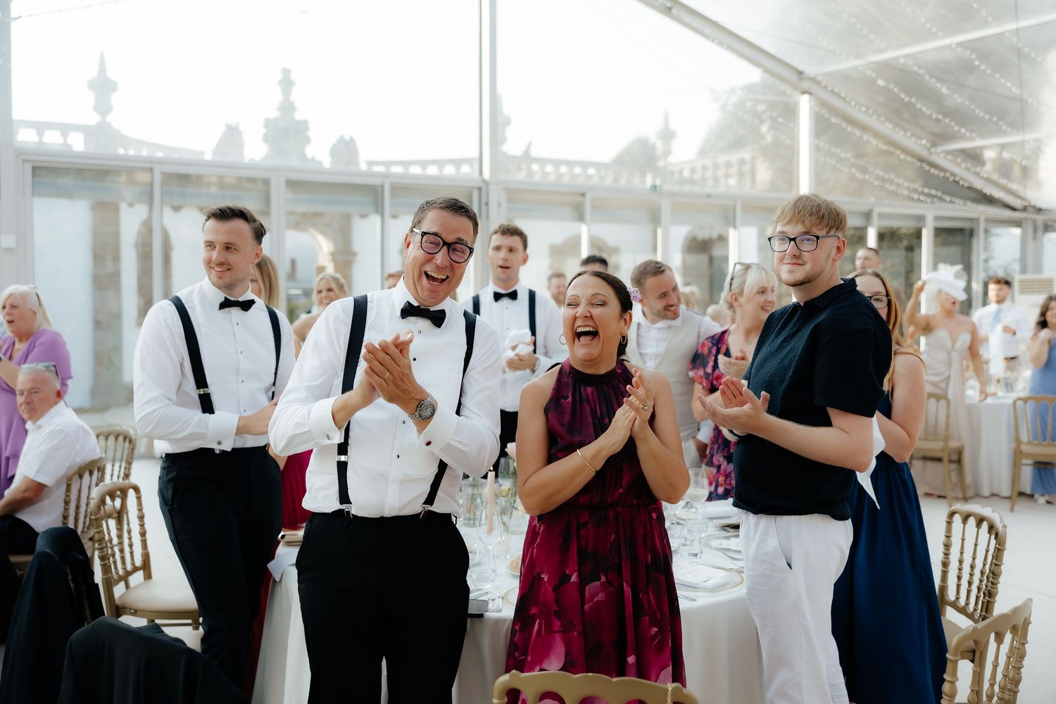 A group of wedding guests react emotionally during a special moment at an indoor reception venue.