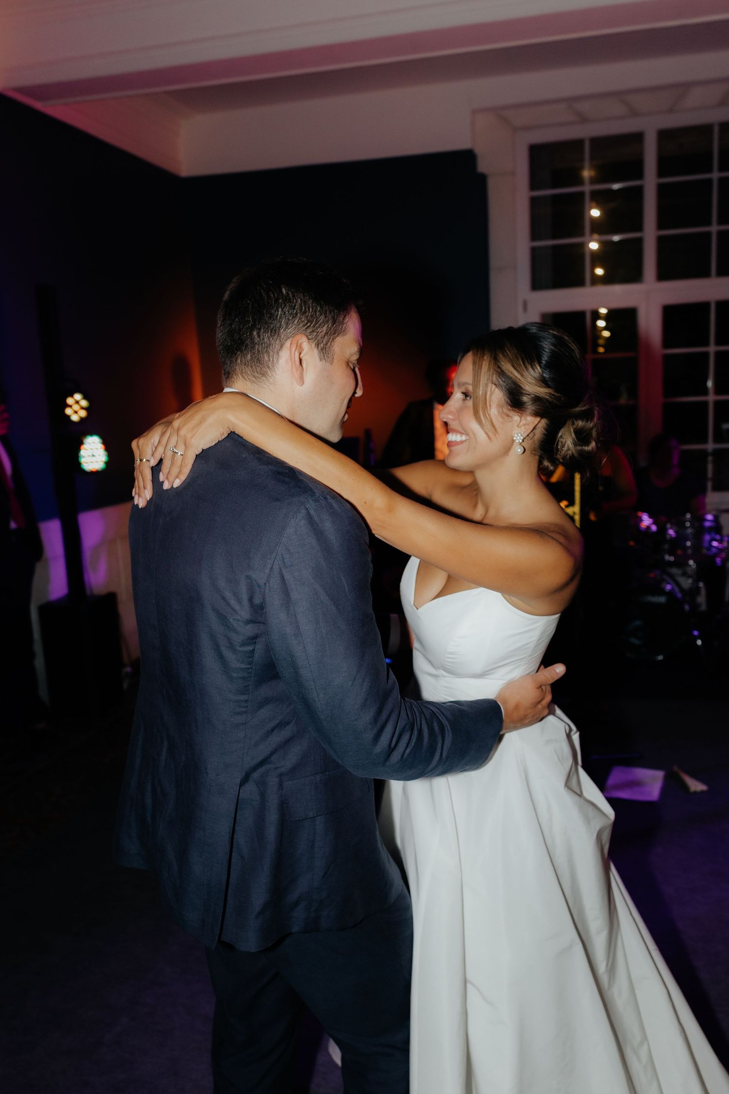 A couple shares a romantic dance at a wedding reception in a dimly lit venue with purple accent lighting.