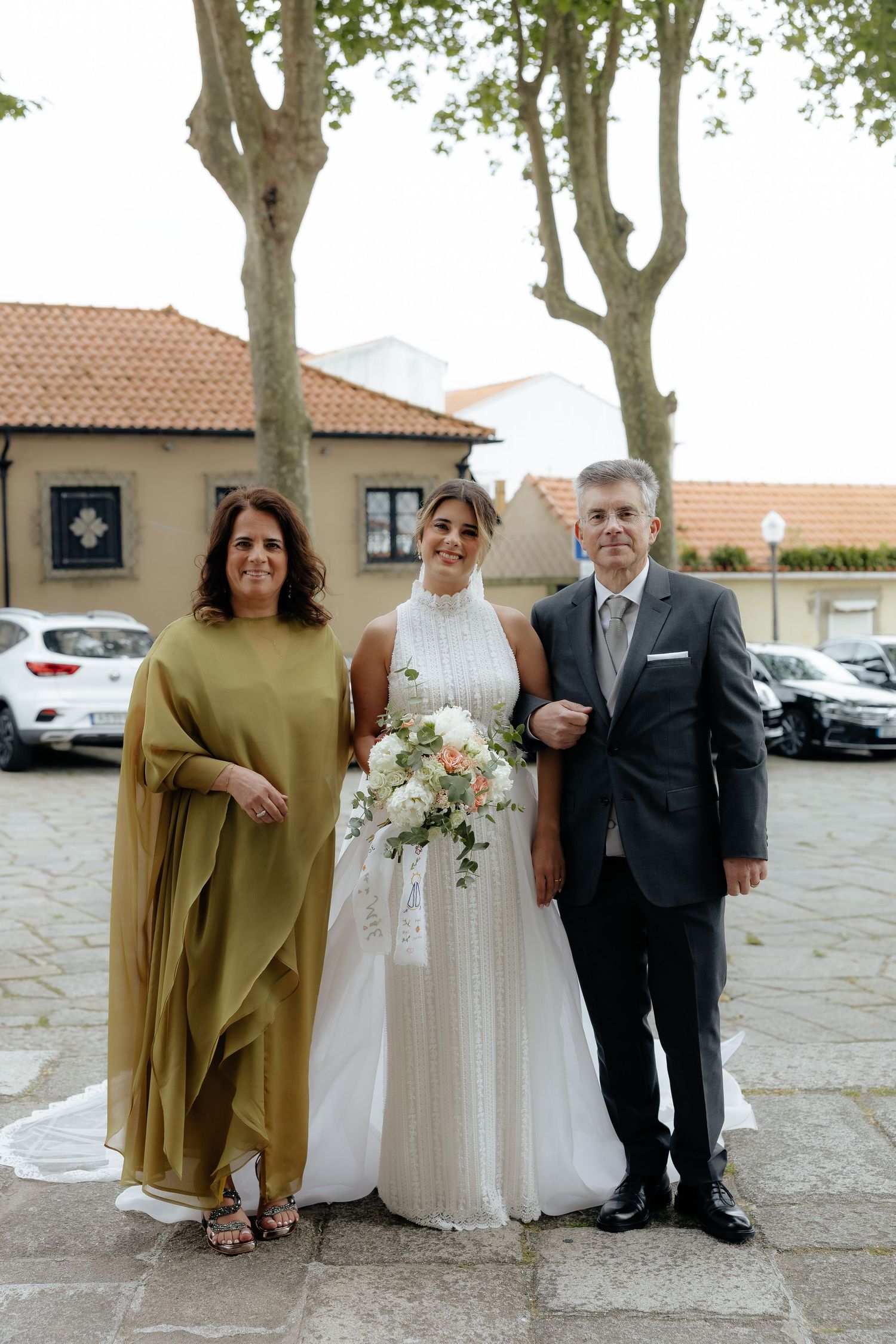 Bride in a white halter gown posing with her parents outdoors before the wedding ceremony.