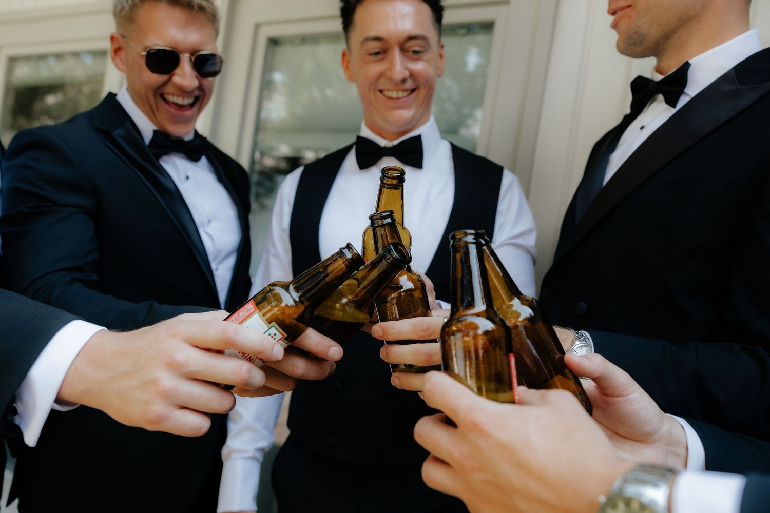 Group of people in formal attire toasting with beer bottles at a celebratory gathering.