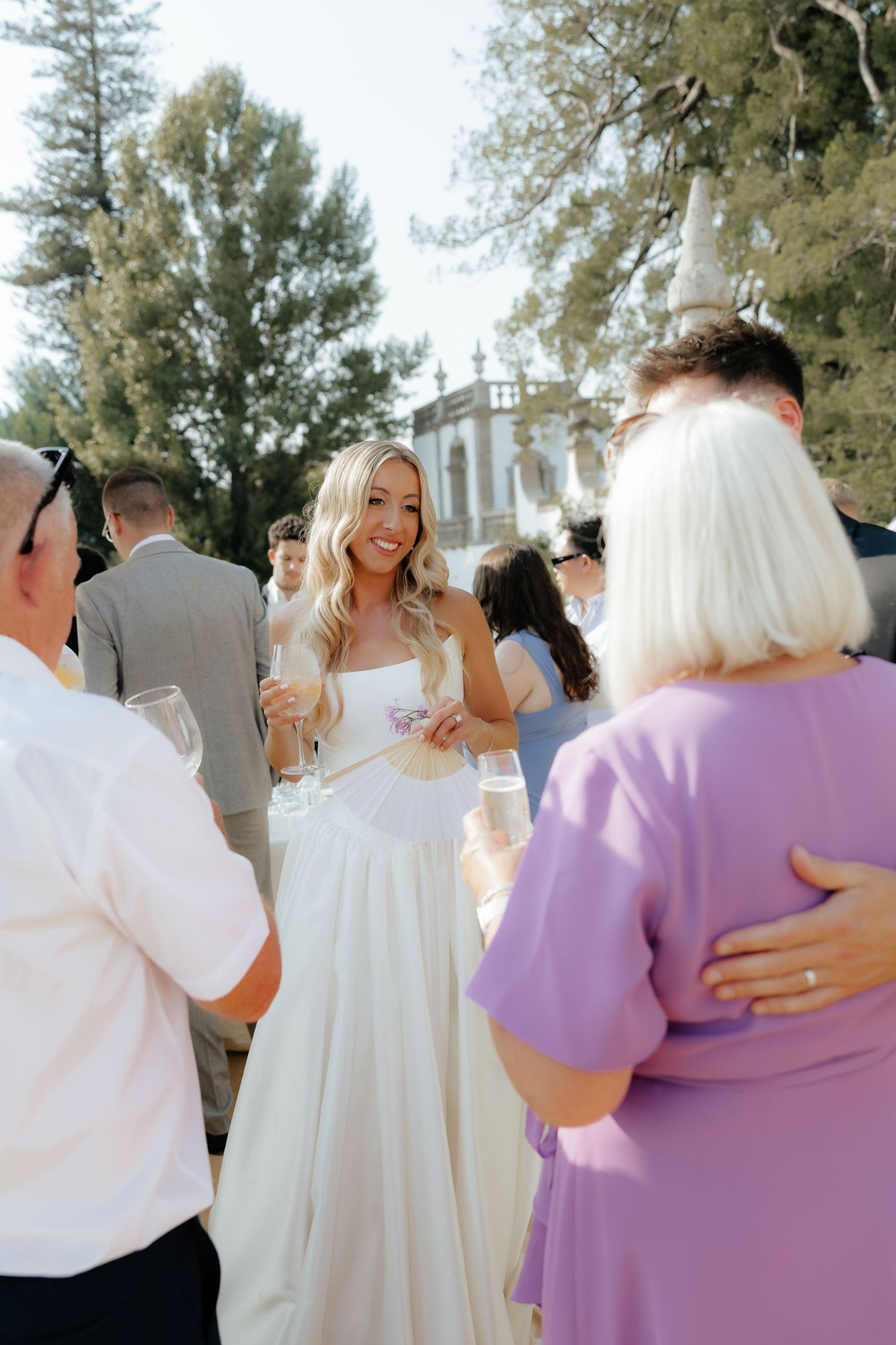 A wedding celebration with guests in white and lavender attire hugging and embracing outdoors.