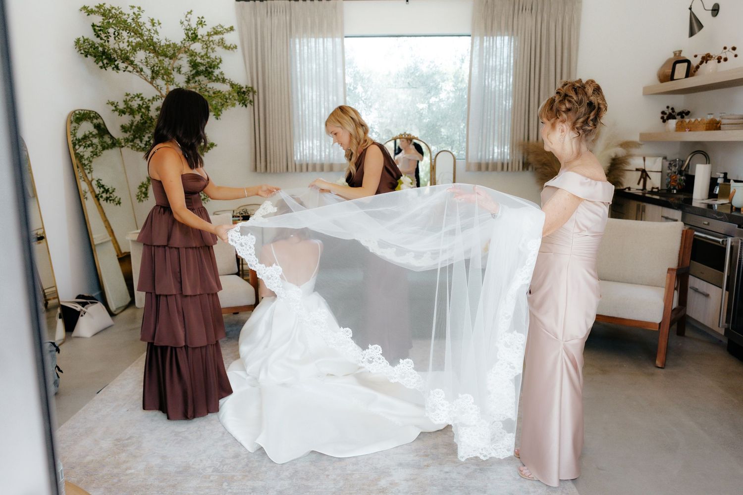 Bridesmaids helping bride with flowing cathedral veil in a bright modern room.