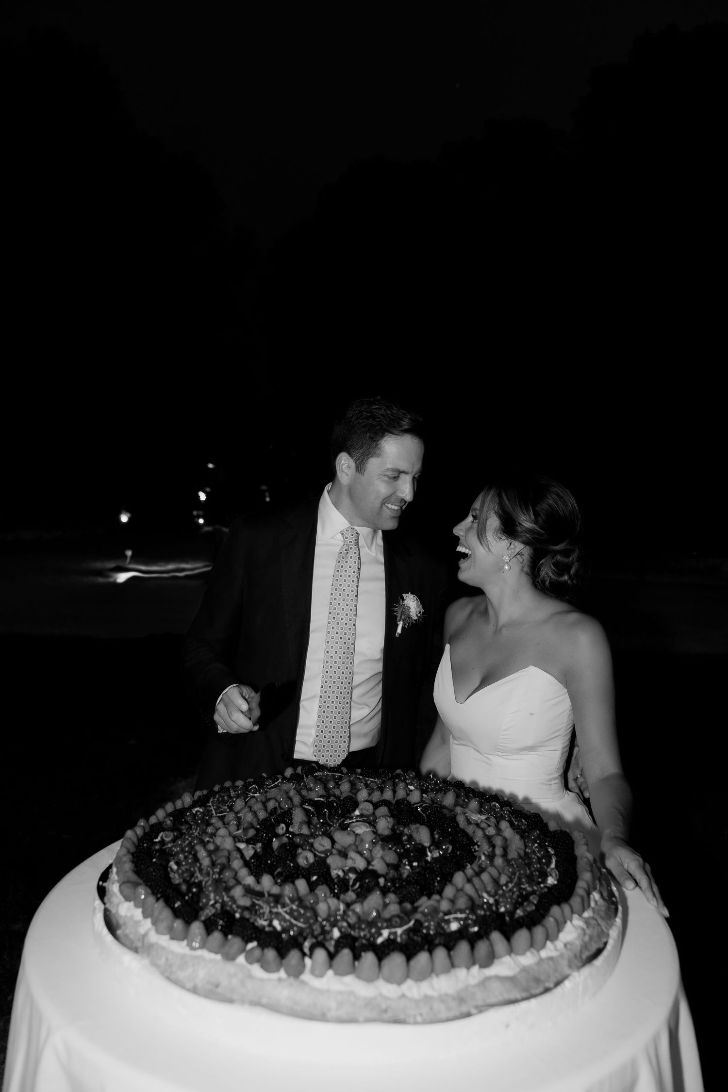 Wedding cake decorated with dark berries displayed at an evening reception.