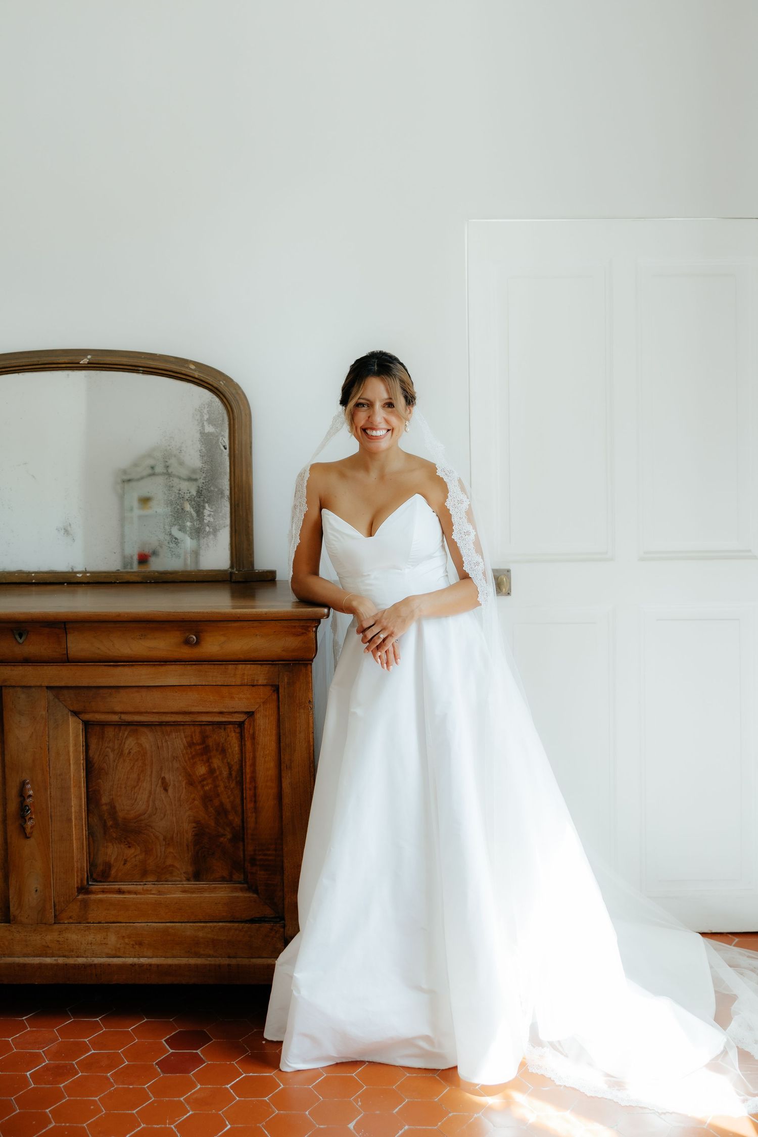 Wedding dress showcased against white walls and wooden vintage furniture in a bridal suite.