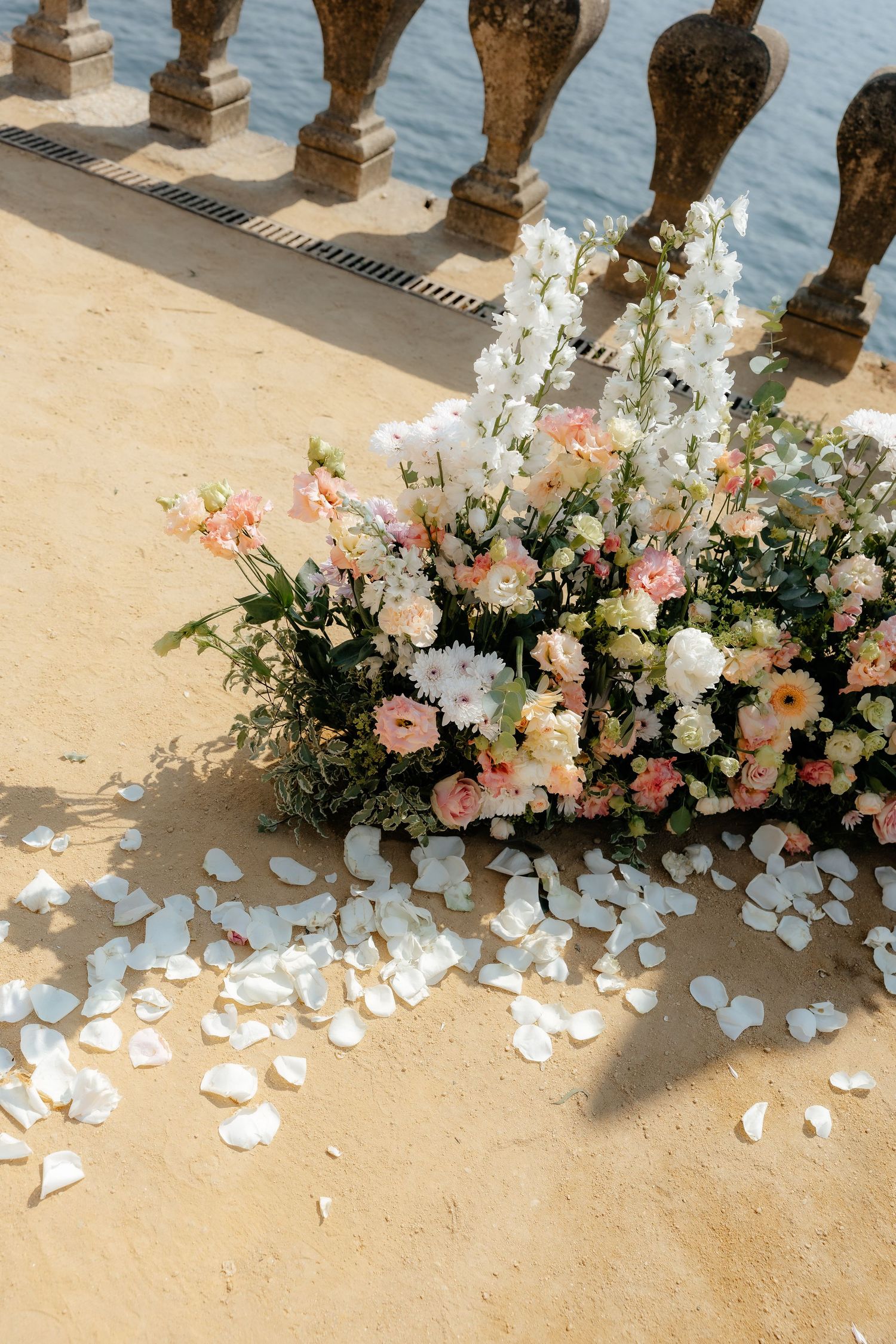 Close-up of lush pink and white wedding flowers with scattered rose petals on a stone terrace.