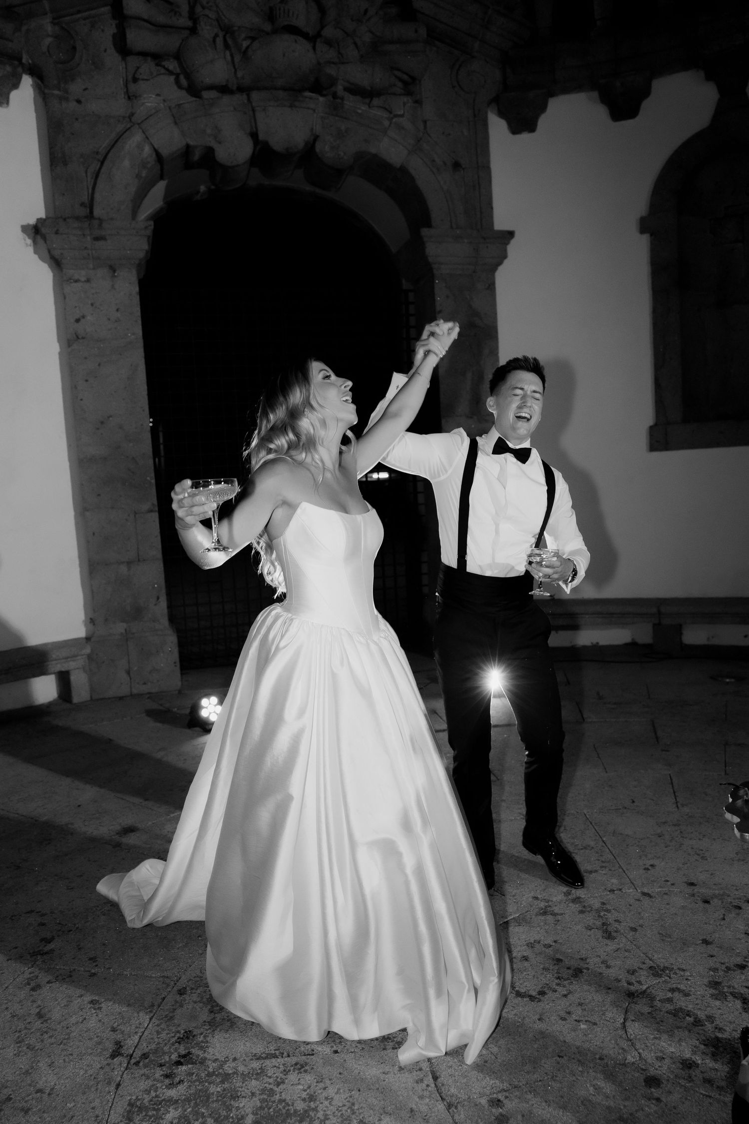 Black and white photo of bride and groom dancing and celebrating joyfully at their wedding reception.