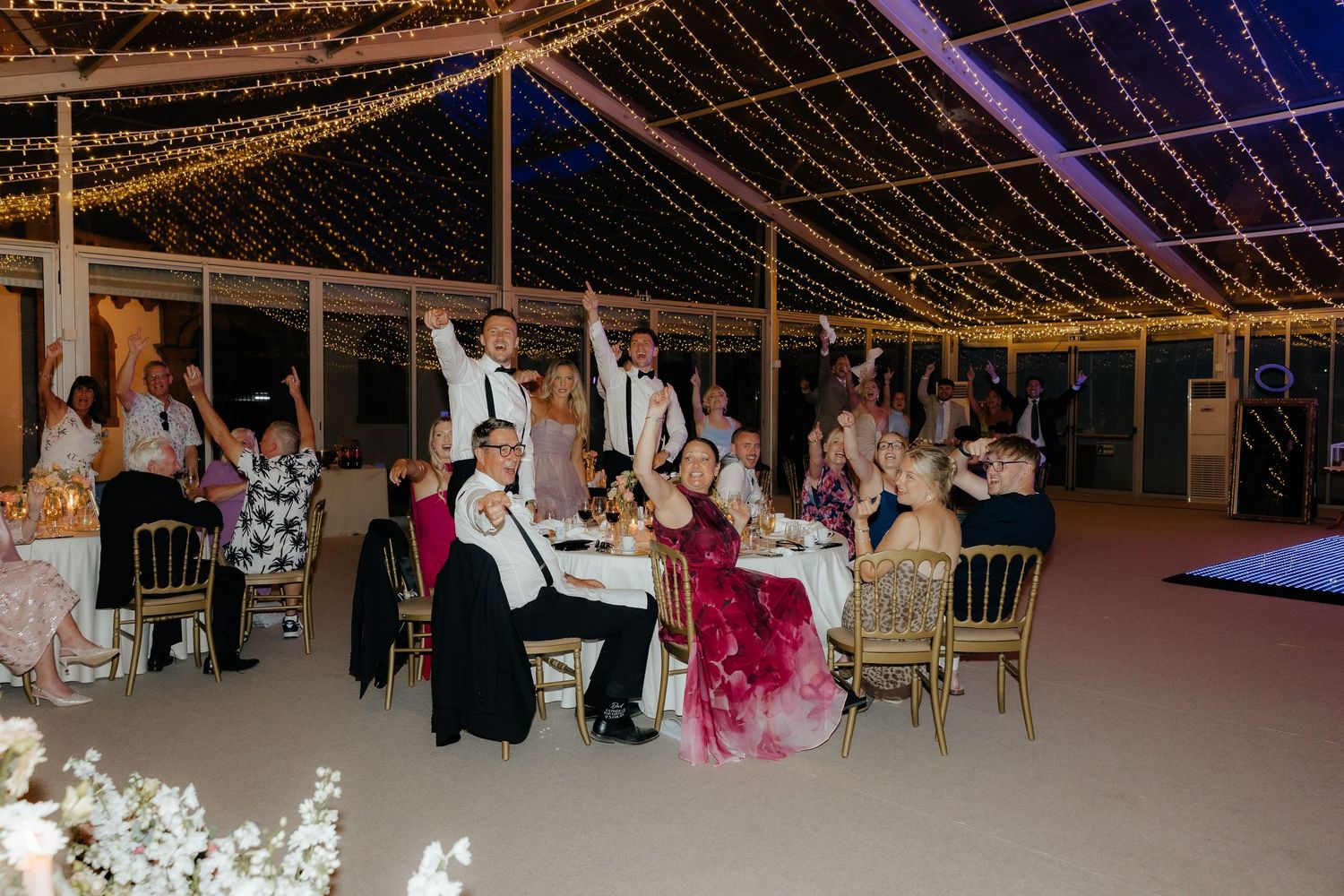Panoramic view of an indoor wedding reception with fairy lights and guests seated at decorated tables.