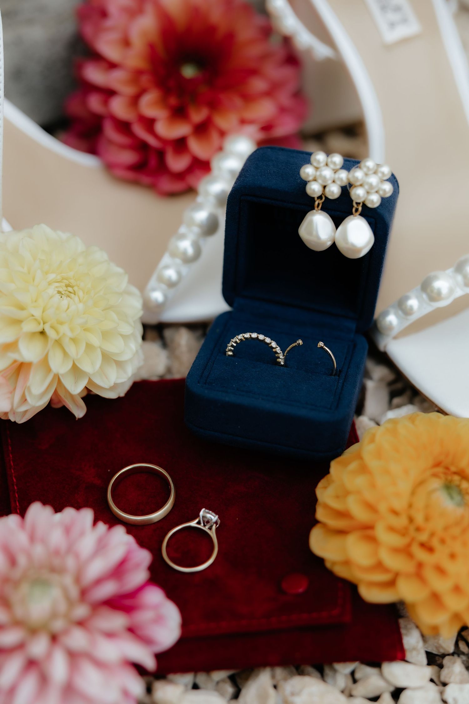 Wedding jewelry and rings displayed with colorful dahlia flowers and navy blue ring boxes.