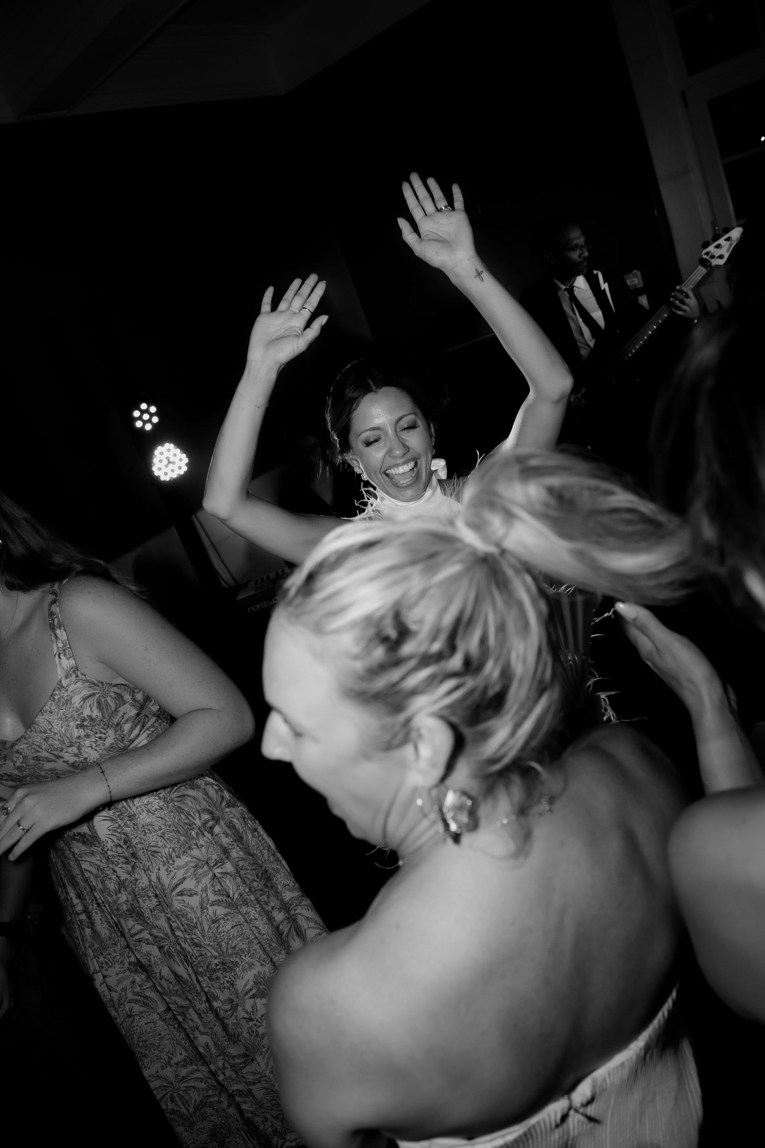 Party guests dance with hands raised on a dark dance floor.
