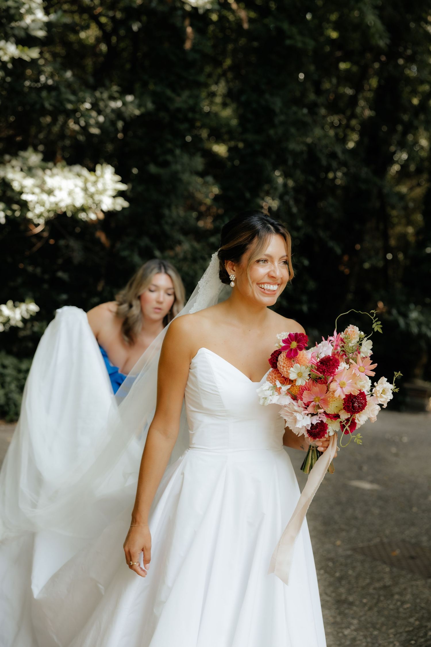 Flowing white wedding gown with colorful bouquet photographed in outdoor setting.