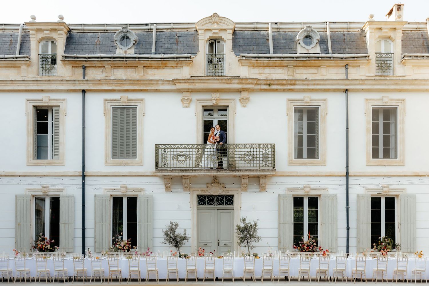 White stone building facade with ornate windows and decorative balconies adorned with colorful flower boxes in European style.