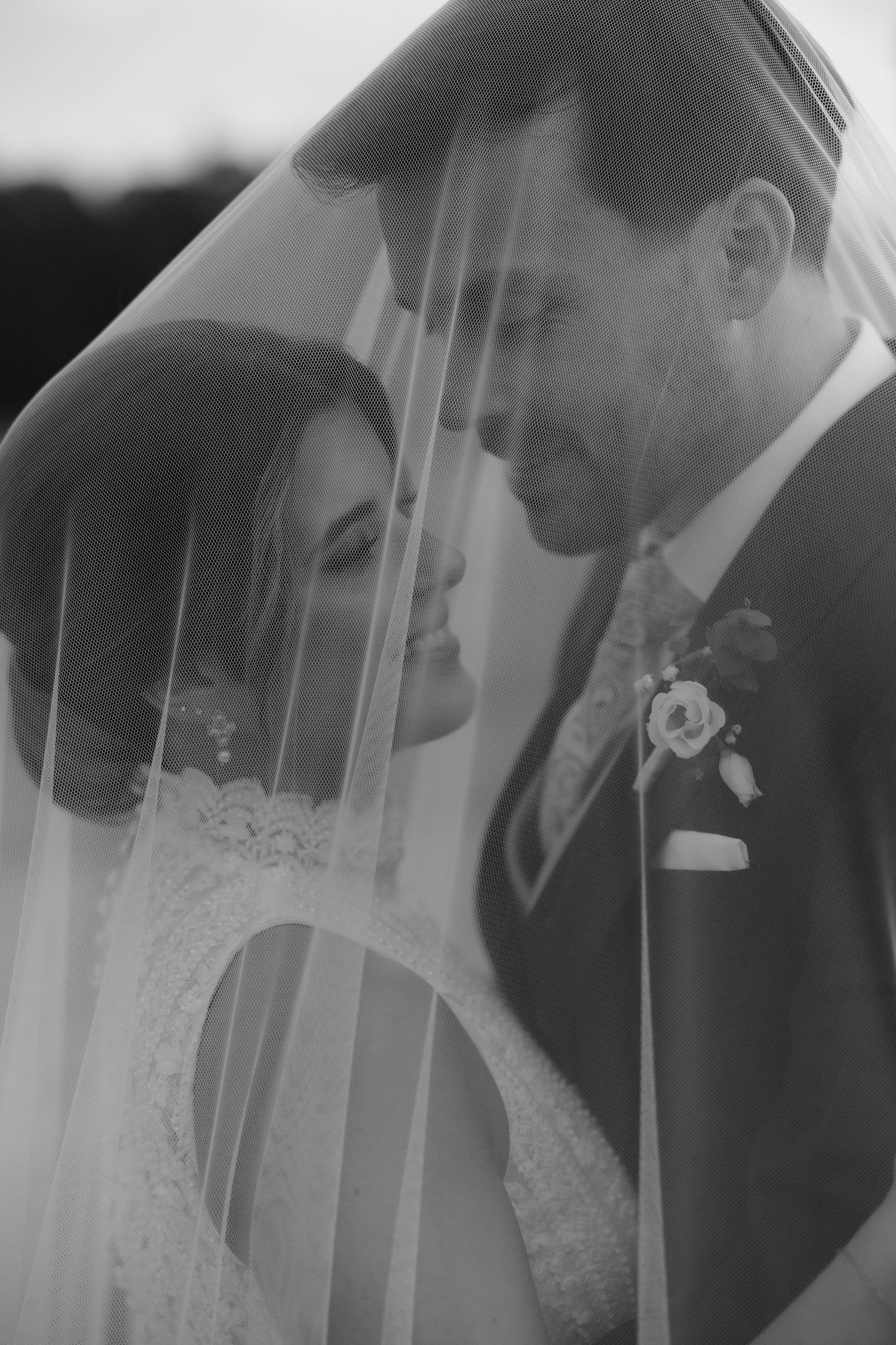 Romantic black and white portrait of bride and groom sharing intimate moment beneath flowing wedding veil.