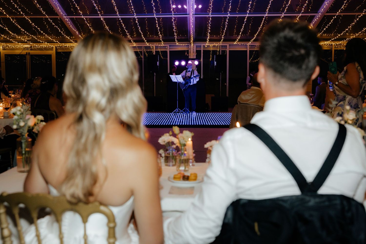 Wedding reception venue decorated with twinkling string lights and elegant table settings under a draped ceiling.