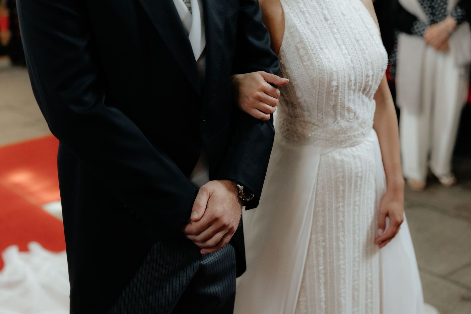Bride and groom hold hands in white wedding dress and dark suit at altar.