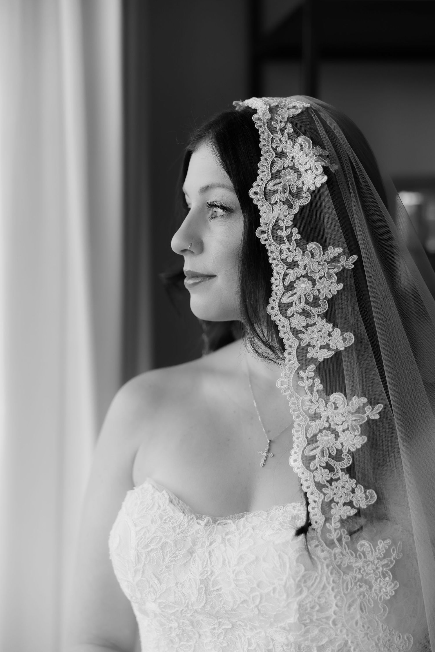 Black and white portrait of a bride wearing a lace veil and strapless gown, gazing thoughtfully to the side.
