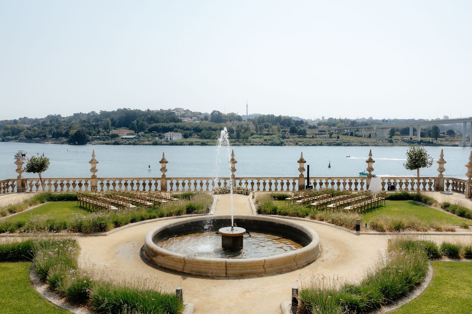 Ornate garden terrace with circular fountain overlooking a scenic coastal bay with stone balustrade railing.