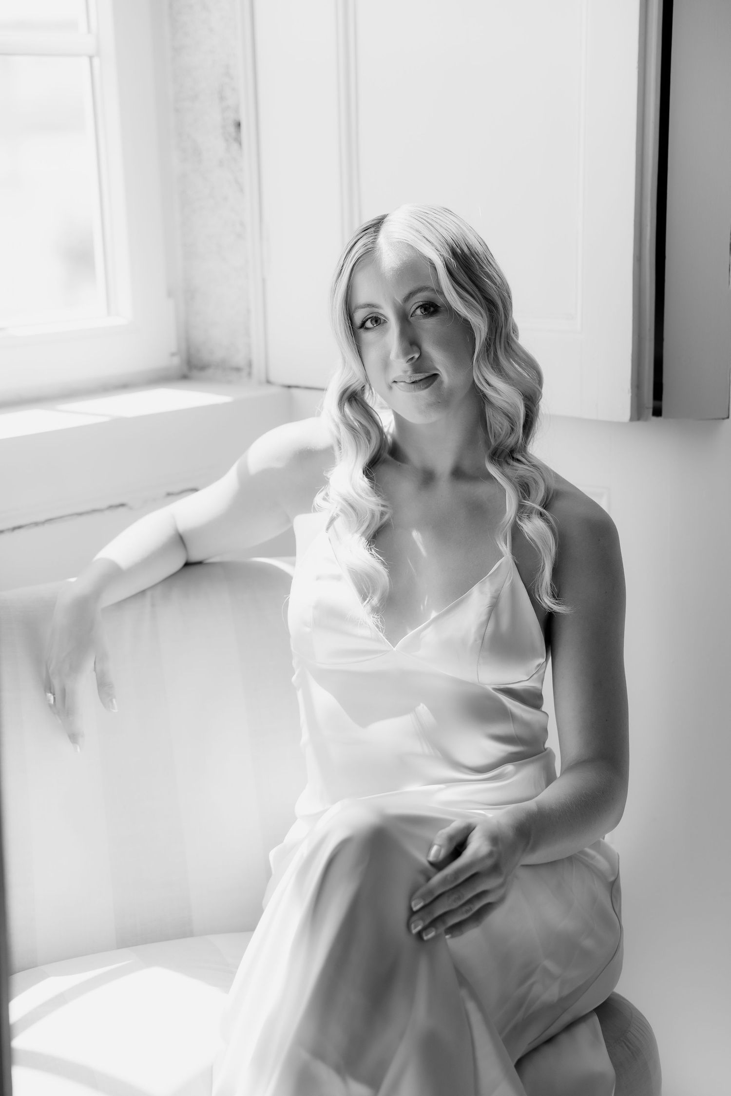 Black and white photo series showing elegant maternity poses near a bright window in soft natural light.