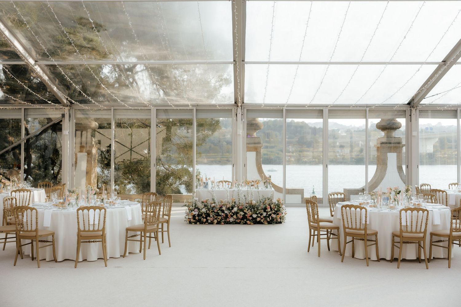Interior view of an elegant white wedding tent with wooden chairs set up for a ceremony or reception.
