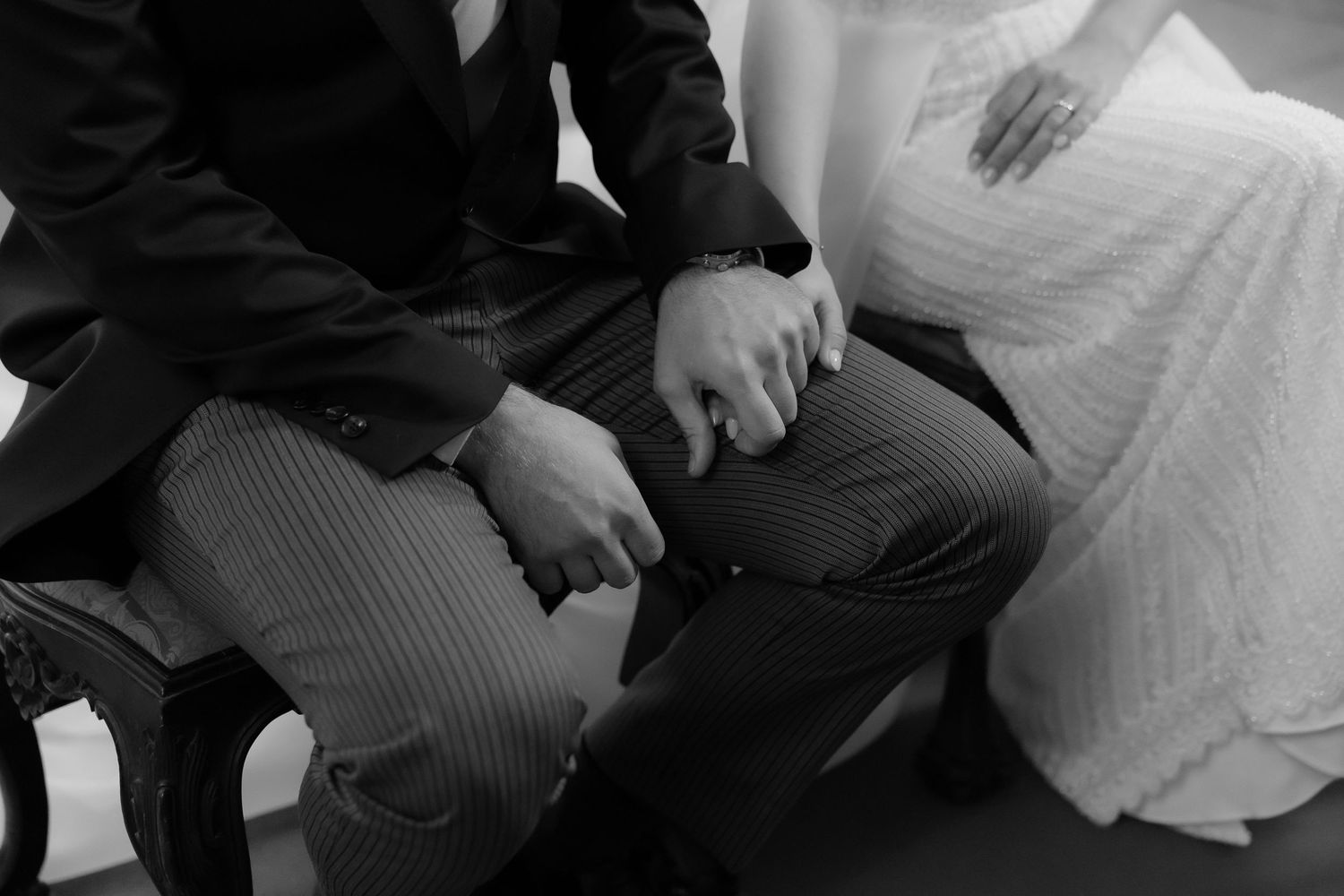 Black and white close-up of bride and groom holding hands during wedding ceremony.