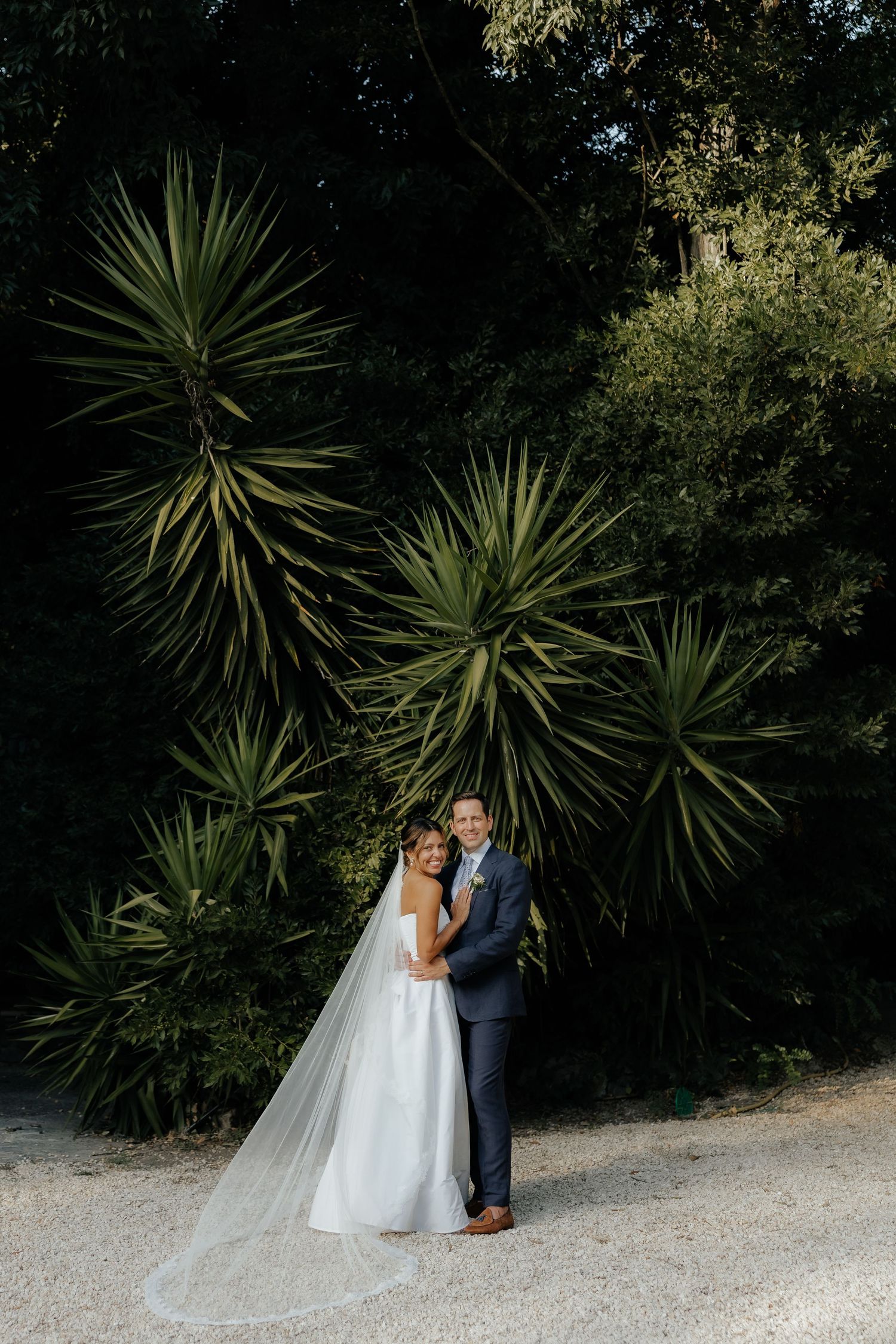 Newlyweds posing for photos against tropical plants on their wedding day.