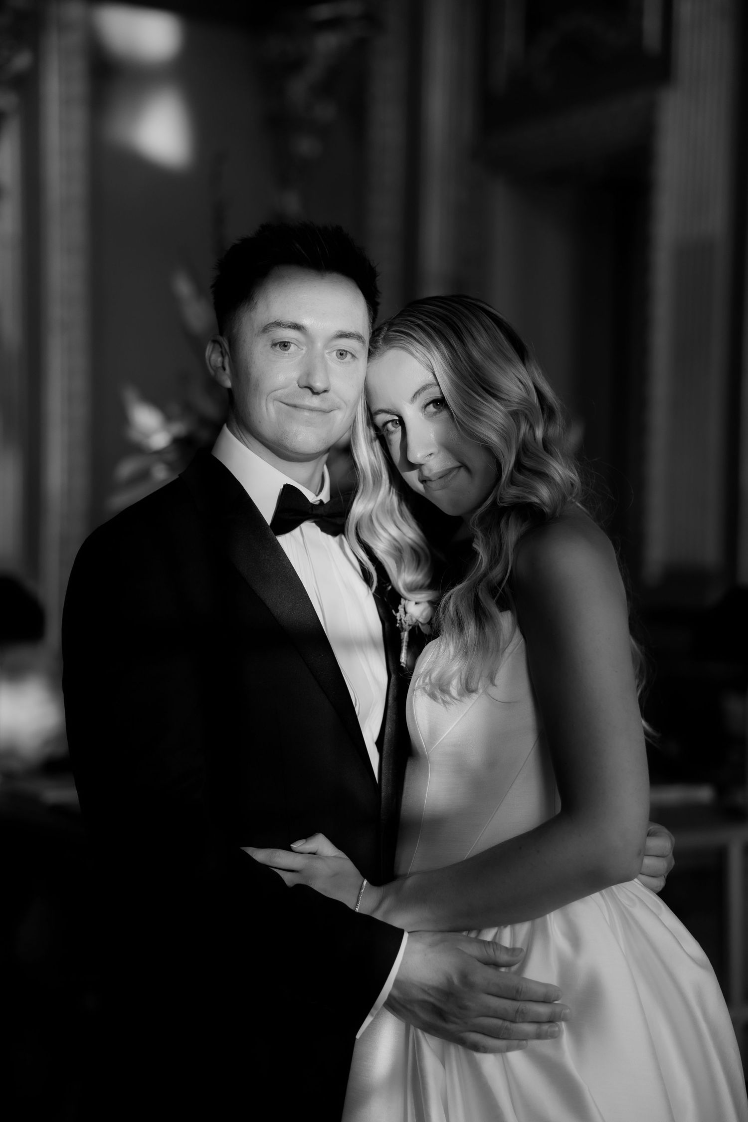 Elegant black and white wedding portrait of a couple in formal attire embracing in romantic lighting.