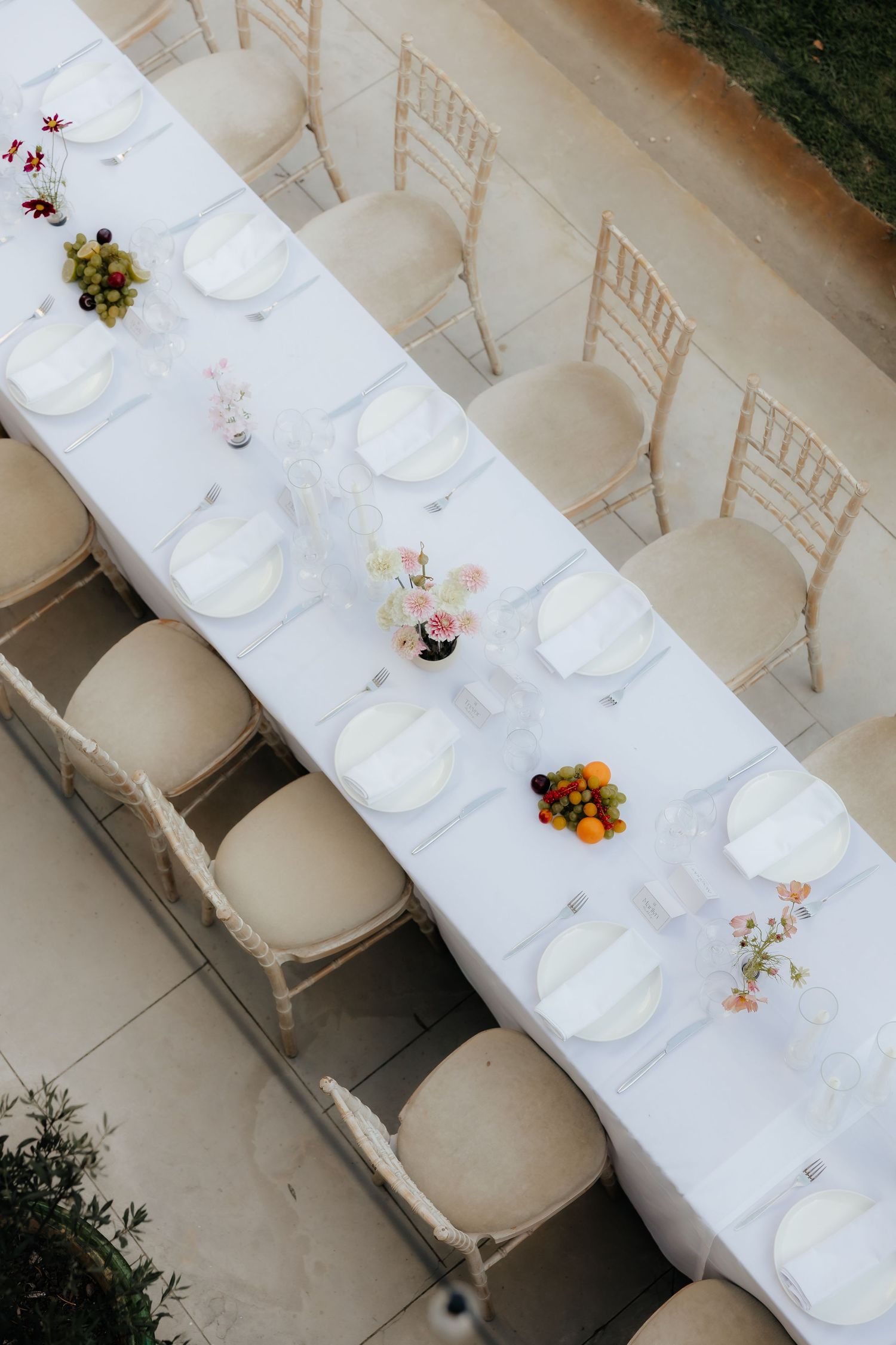 Overhead view of long white dining table with cream chairs and minimalist floral centerpieces.