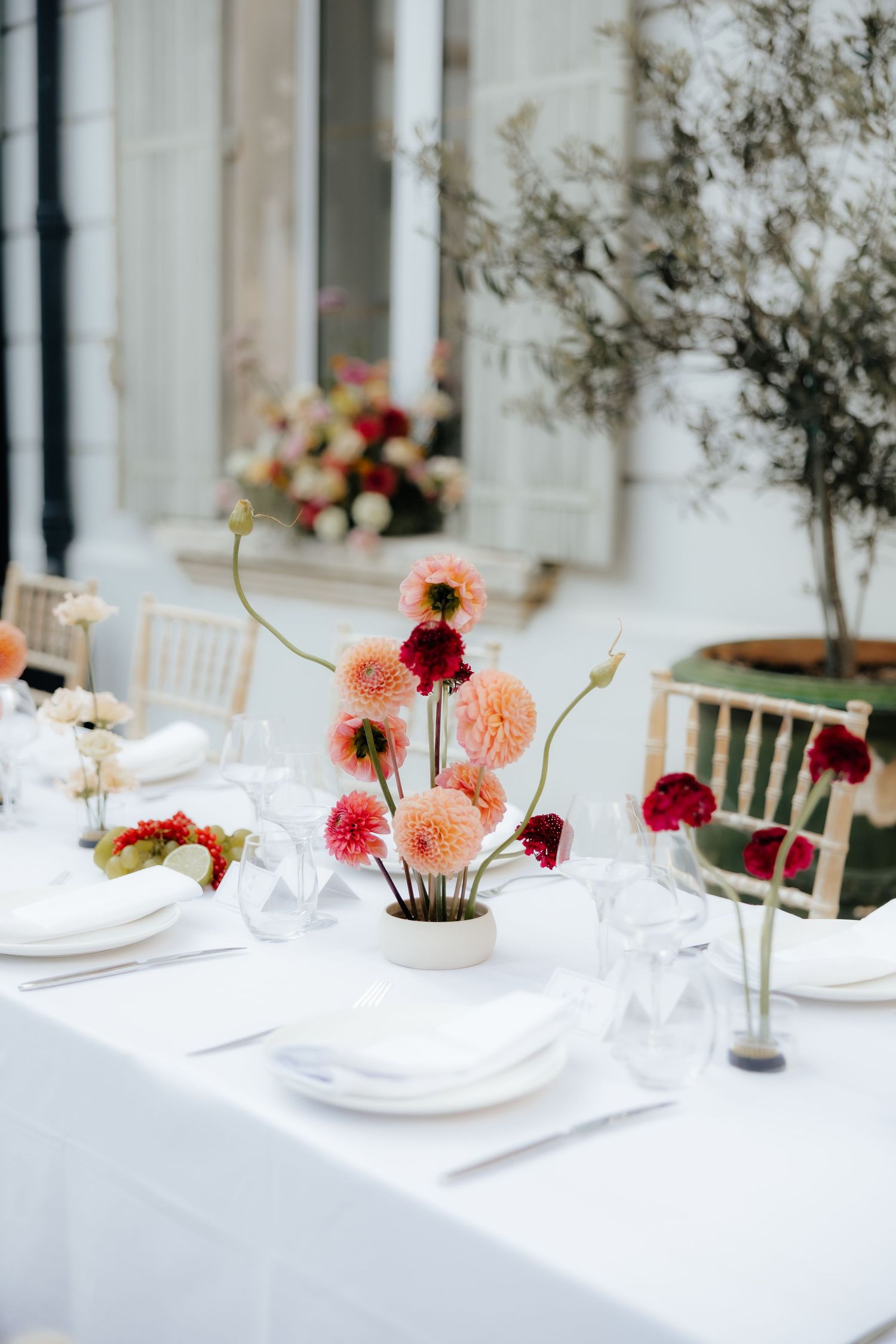 Elegant table setting with pink and burgundy dahlia flowers in small vases on white tablecloth.