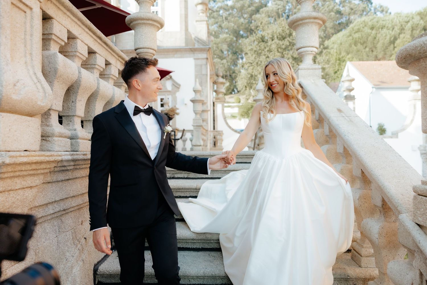 A romantic wedding photoshoot featuring a couple dancing and twirling in an elegant outdoor setting with stone architecture.