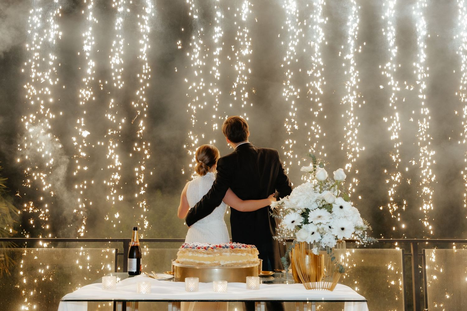 Bride and groom embracing before stunning cascading sparkler backdrop at wedding reception.